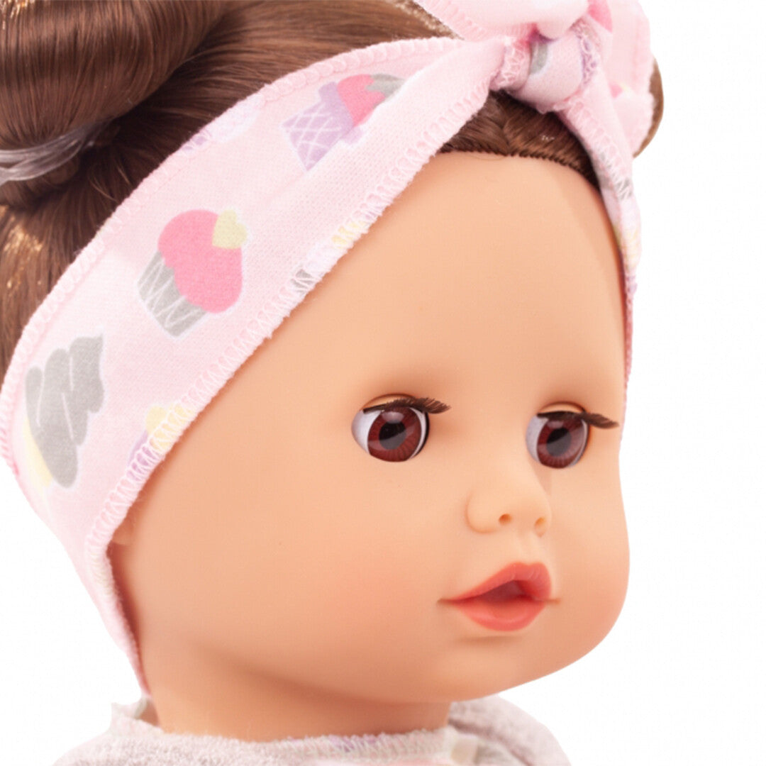 Close-up van het gezicht van de babypop met bruine ogen en een roze hoofdband met cupcake-patroon.