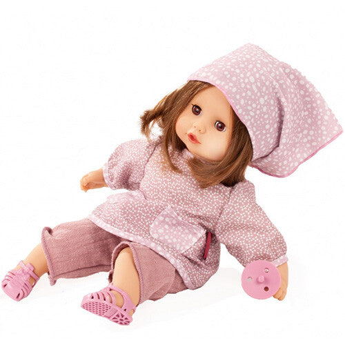 Götz babypop Muffin Soft Mood met bruin haar, roze kleding met stippen en roze sandalen, liggend met een roze speen naast de hand.