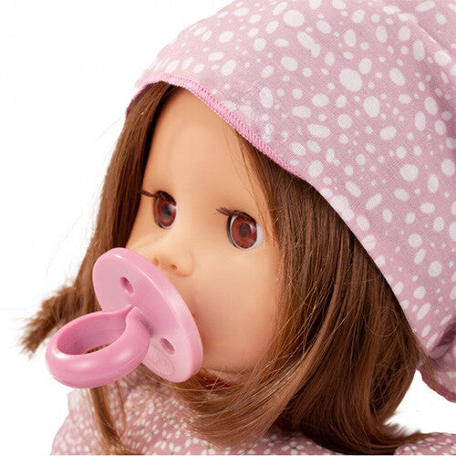 Close-up van het gezicht van de Götz babypop Muffin Soft Mood met bruin haar, bruine ogen en een roze speen in de mond.