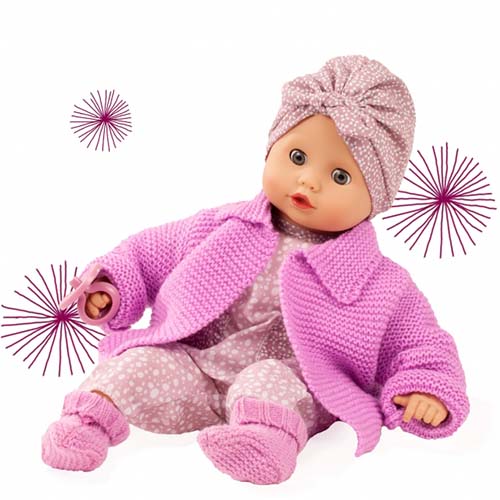 Götz babypop Muffin Soft Mood met roze gebreid vestje, stippenpakje en bijpassende hoofdband, zittend met speen in de hand.