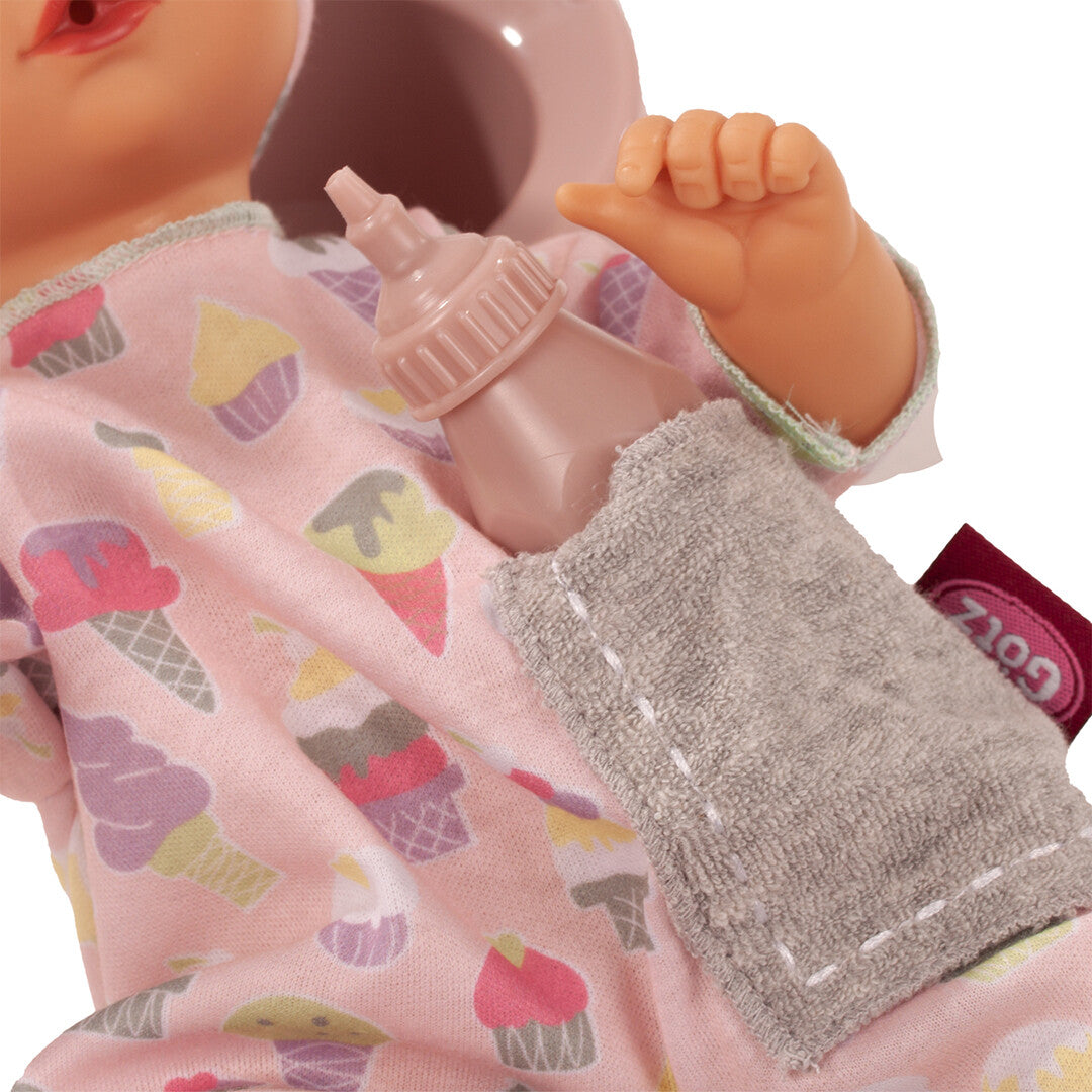 Detail van de Götz bad- en plaspop met roze outfit met ijsjespatroon, een flesje en een doekje.