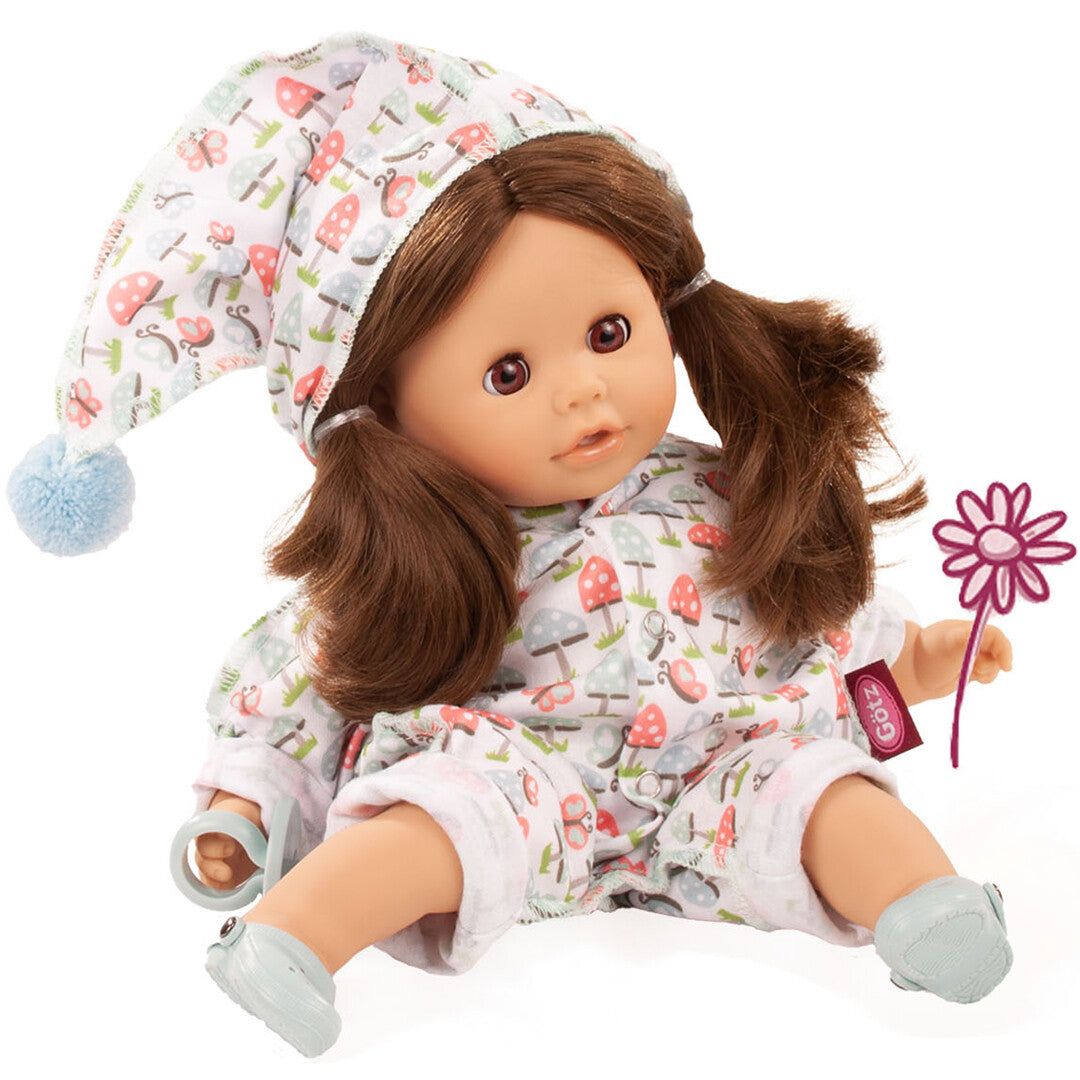 Gotz badpop met bruine pigtails, zittend in een wit slaappakje met paddenstoelenpatroon en bijpassende muts, een roze bloem vasthoudend.