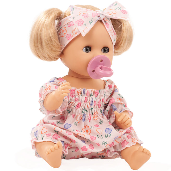 Götz badpop met blond haar, roze gebloemde outfit, hoofdband en roze speen, zittend van voren.