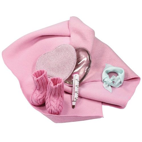 Een collectie götz poppenaccessoires, waaronder roze gebreide slofjes, een thermometer en hartvormige kruiken, liggend op een roze deken.