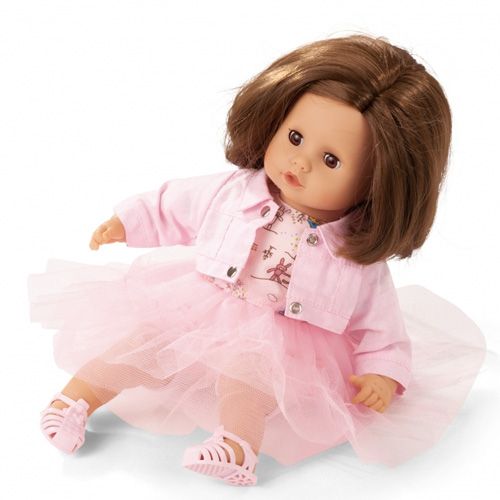 Een pop met bruin haar draagt de Gotz roze poppenkledingset met jurk, jasje en sandalen.