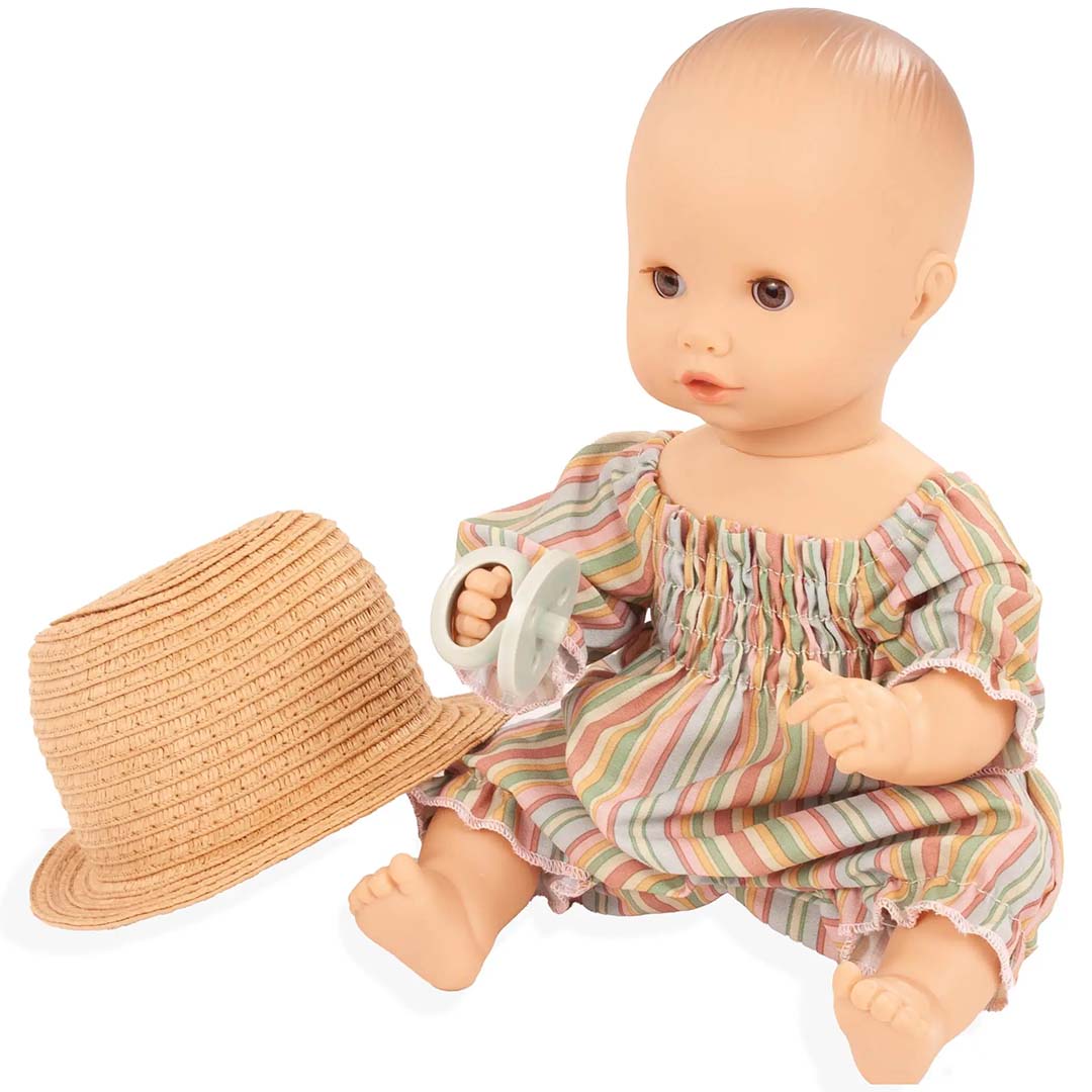 Götz bad- en plaspop Sleepy Aquini met gestreepte outfit en speen in de hand, met een strohoed ernaast.