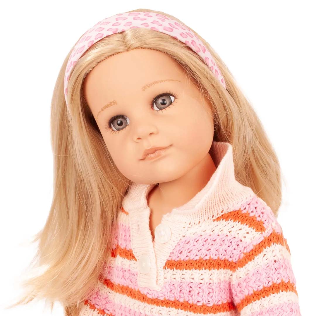 Een Gotz pop met lange blonde haren draagt een roze luipaardprint haarband en een gestreepte trui.