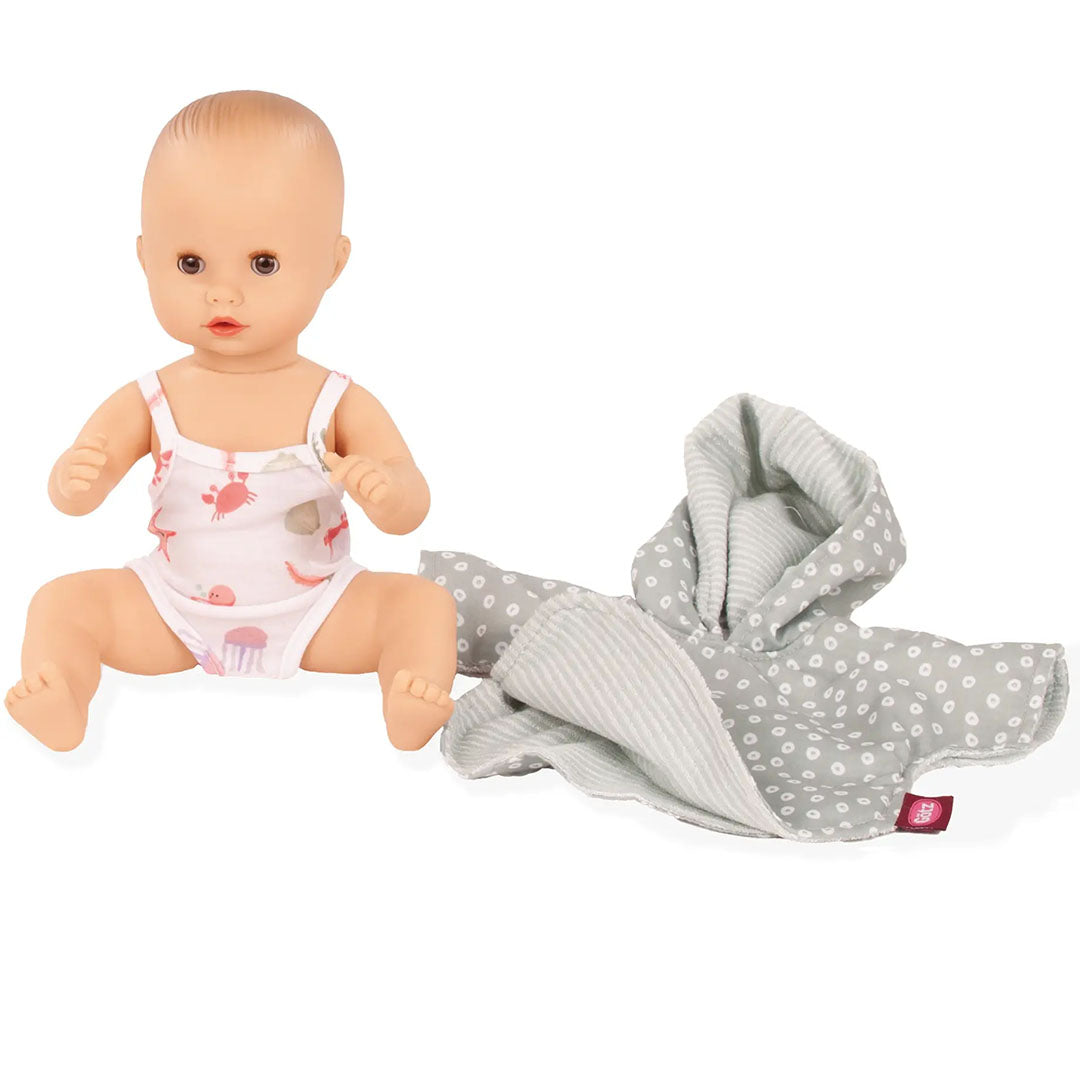 Babypop draagt een wit badpak met zeedieren, met de Götz grijze poncho ernaast.