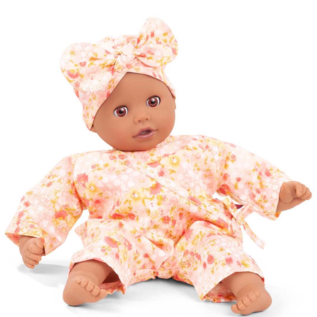 Gotz poppenkleding set met roze gebloemde jumpsuit en hoofdband gedragen door een zittende babypop.