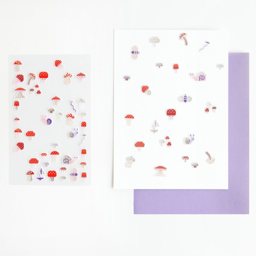 Diverse pixel paddenstoel gelstickers geplakt op twee witte vellen papier, met een paarse envelop ernaast.