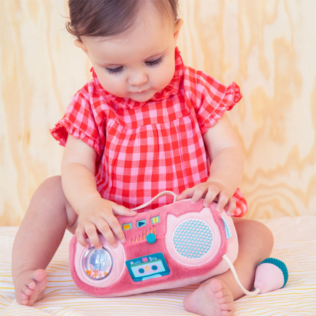 Een baby speelt zittend met de roze pluche activiteitenradio in de vorm van een kat.