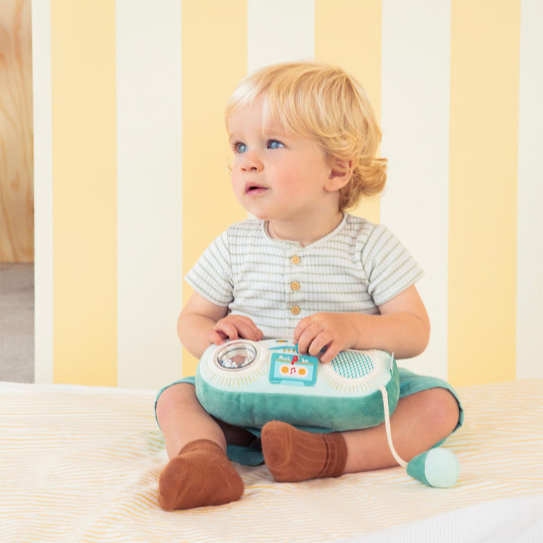 Een baby zit op een deken en speelt met de Lilliputiens groene activiteitenradio.
