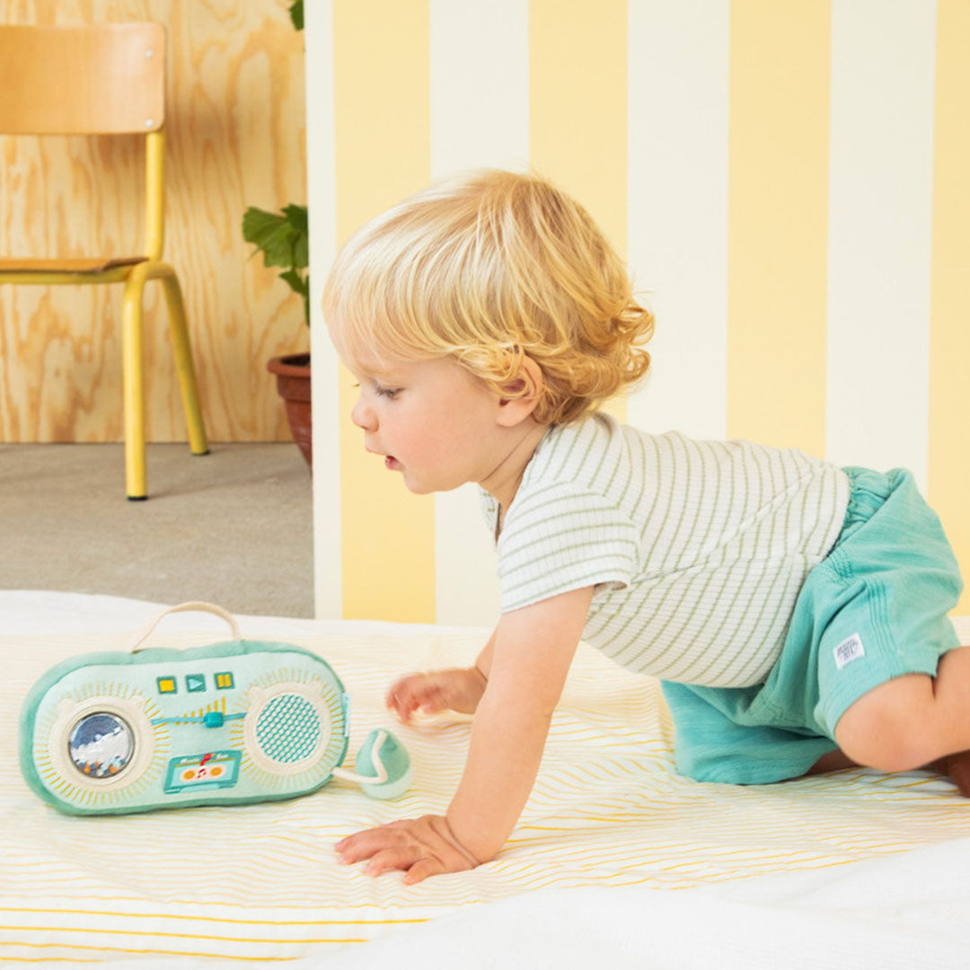 Een baby kruipt op een deken naar de Lilliputiens groene activiteitenradio.