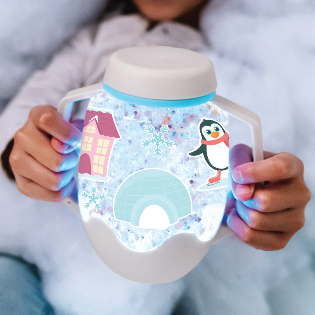 Een kind houdt een gloeiende glo pals speelbeker vast met een pinguïn, iglo en sneeuwvlokken erin.