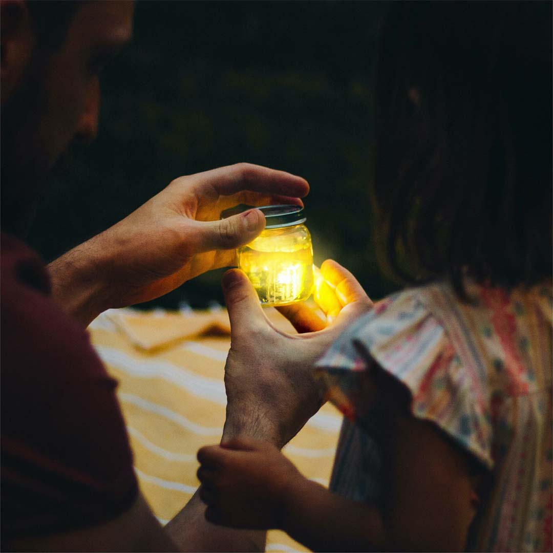 Een volwassene en een kind houden samen een lichtgevende pot vast in het donker.