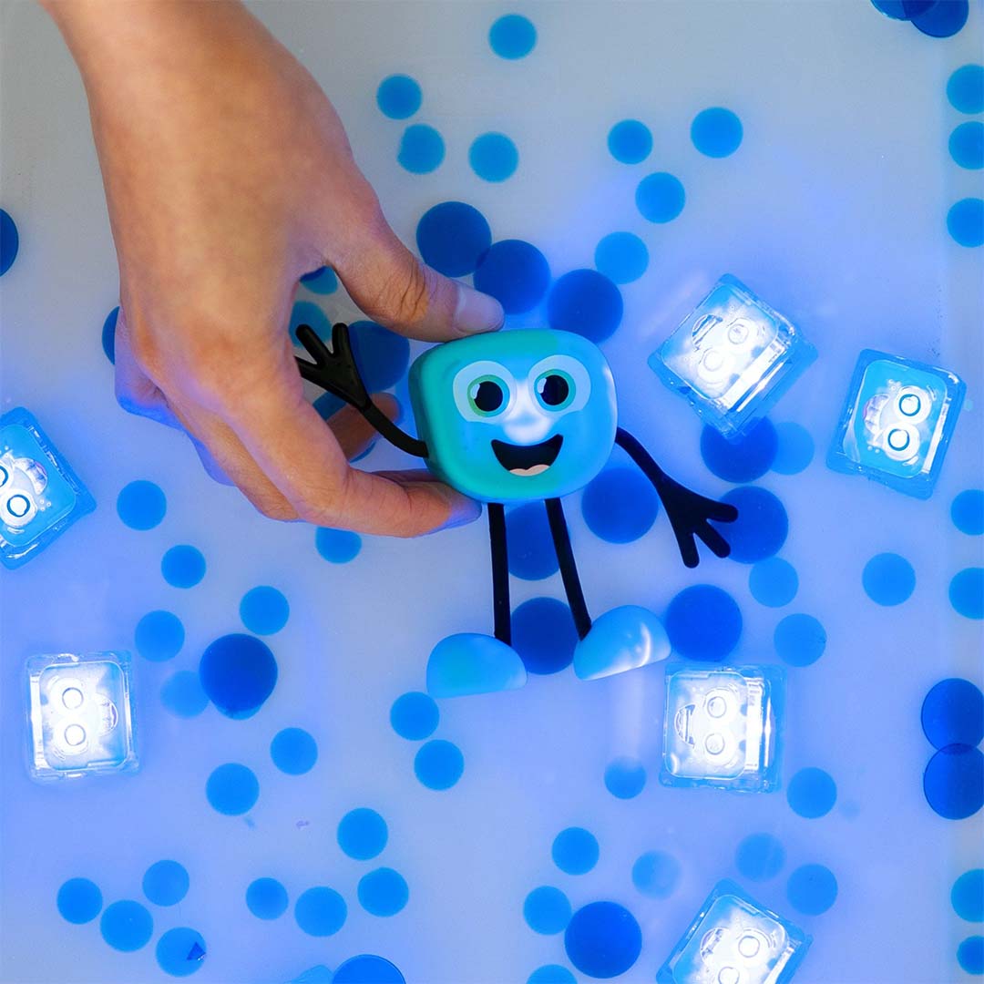 Een hand houdt het glo pals Blair badspeelgoed in water met oplichtende blokjes en blauwe decoratie.