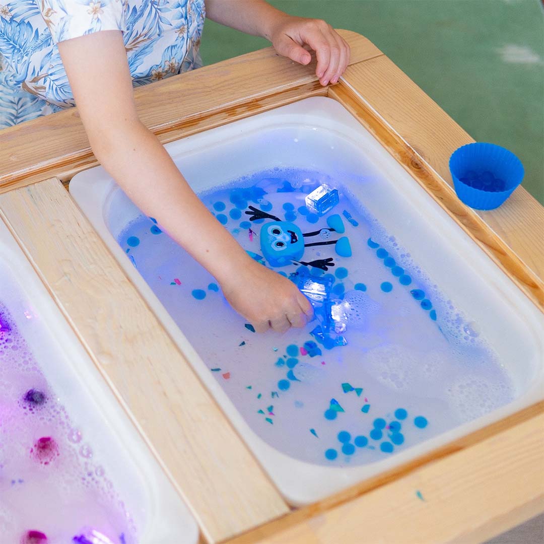Een kind speelt met het glo pals Blair badspeelgoed en lichtgevende blokjes in een watertafel.
