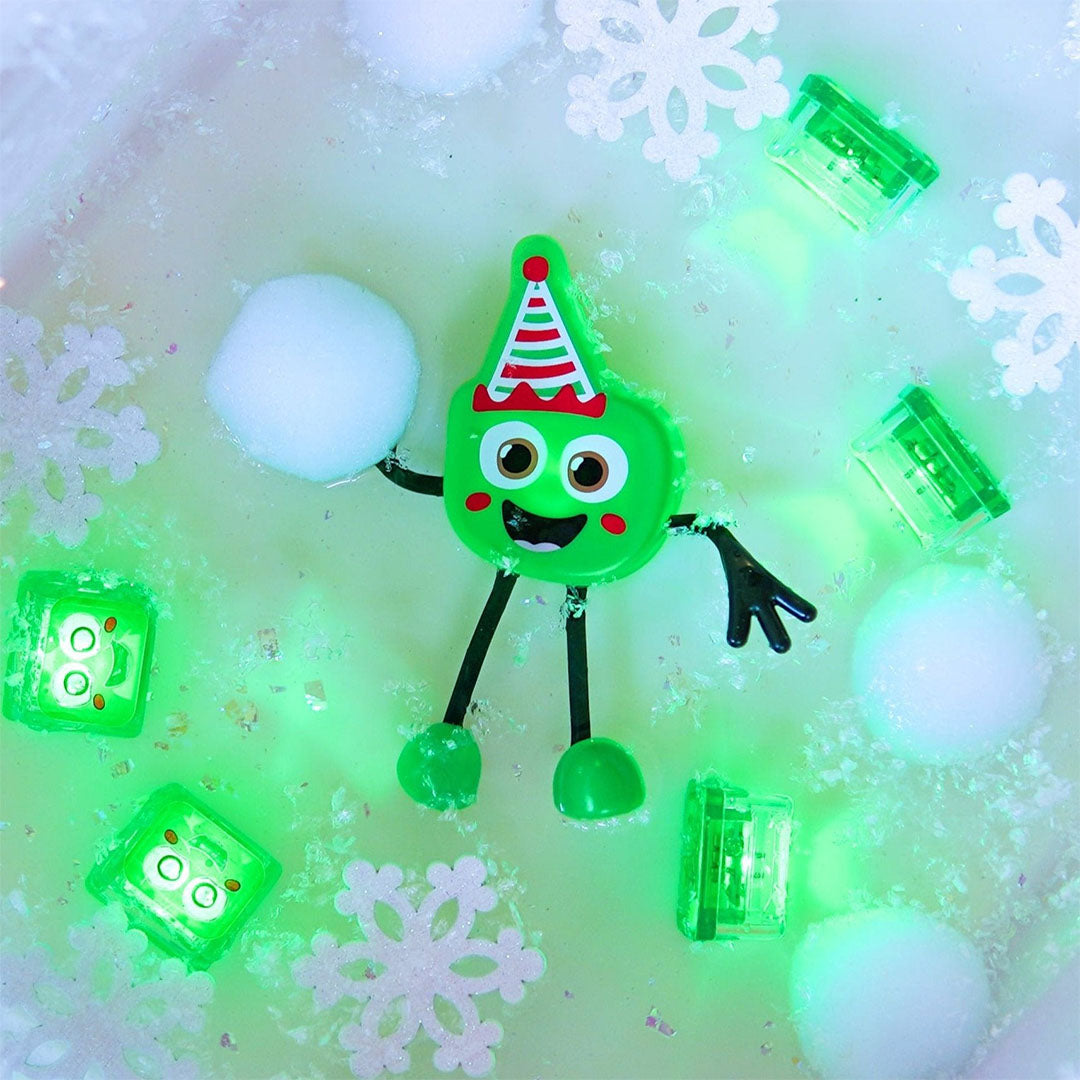 Glo Pals groen kerst badspeelgoed figuurtje in water, omringd door lichtgevende blokjes en sneeuwvlokken.