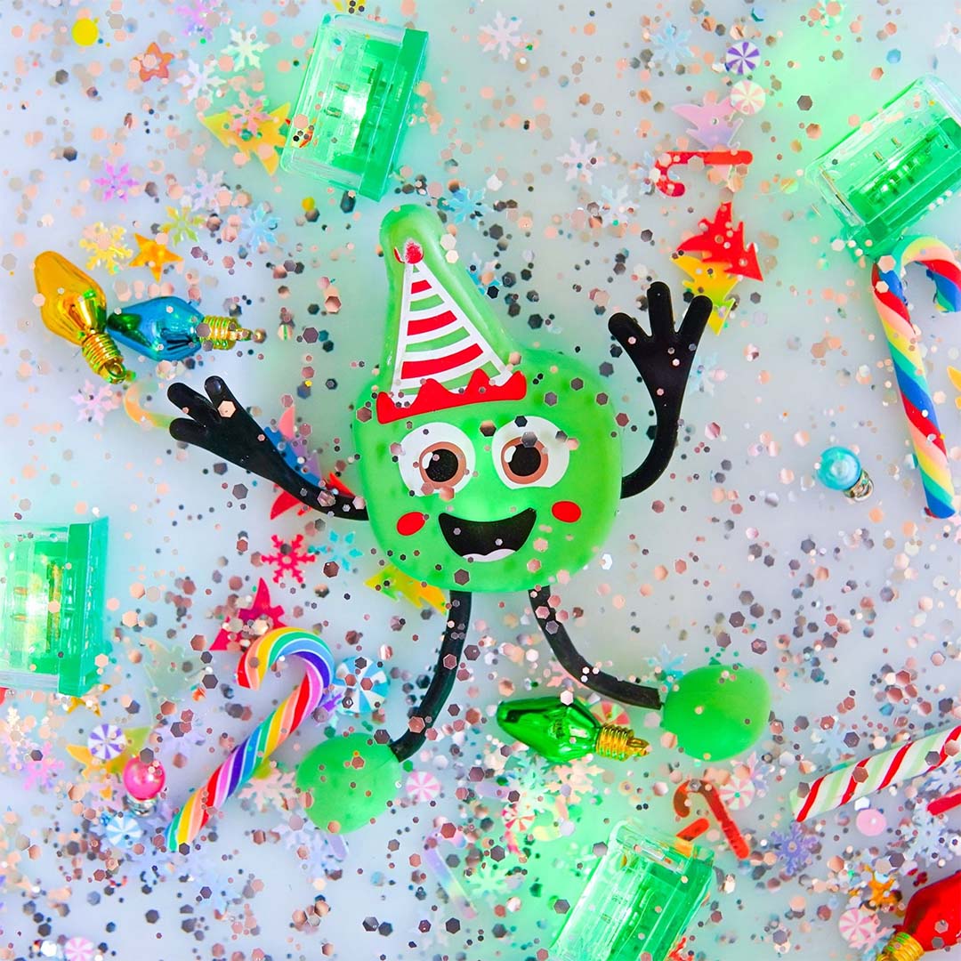 Glo Pals groen kerst badspeelgoed figuurtje op een glimmende ondergrond met confetti, zuurstokken en lichtgevende blokjes.