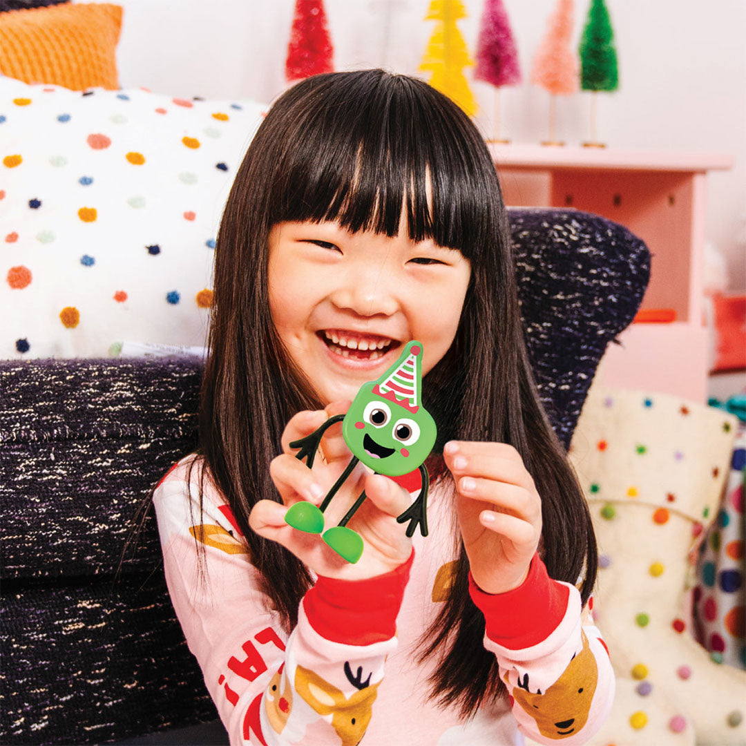 Een lachend kind houdt het Glo Pals groene kerst badspeelgoed figuurtje met feestmuts vast.