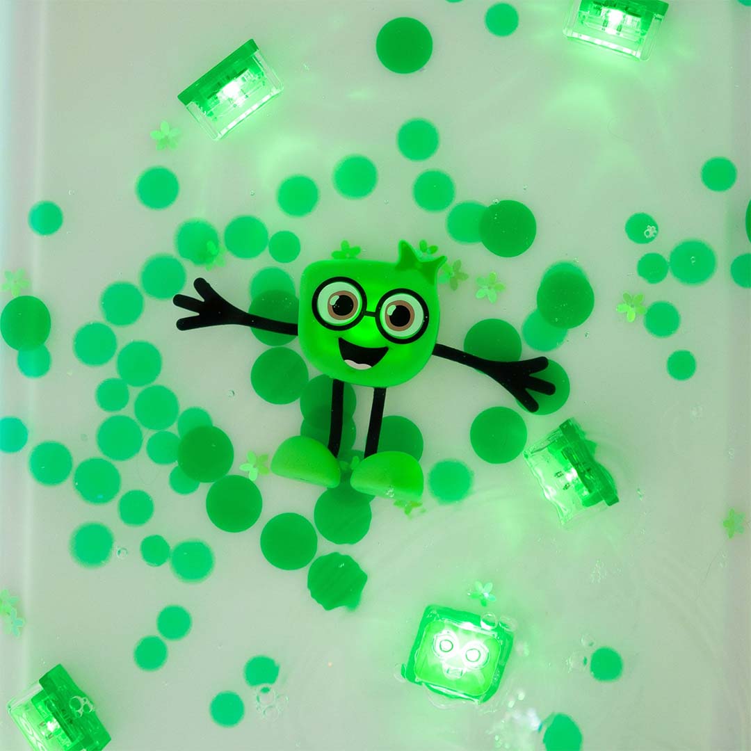 De groene Glo Pals Pippa badspeelgoedfiguur drijft in het water, omringd door lichtgevende groene blokjes en confetti.