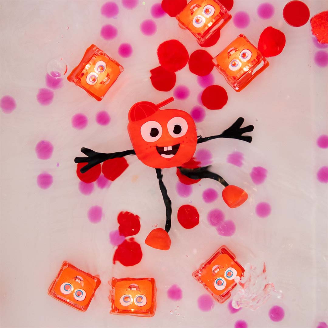 Het glo pals badspeelgoed Sammy en meerdere lichtgevende blokjes drijven in badwater met roze en rode stippen.