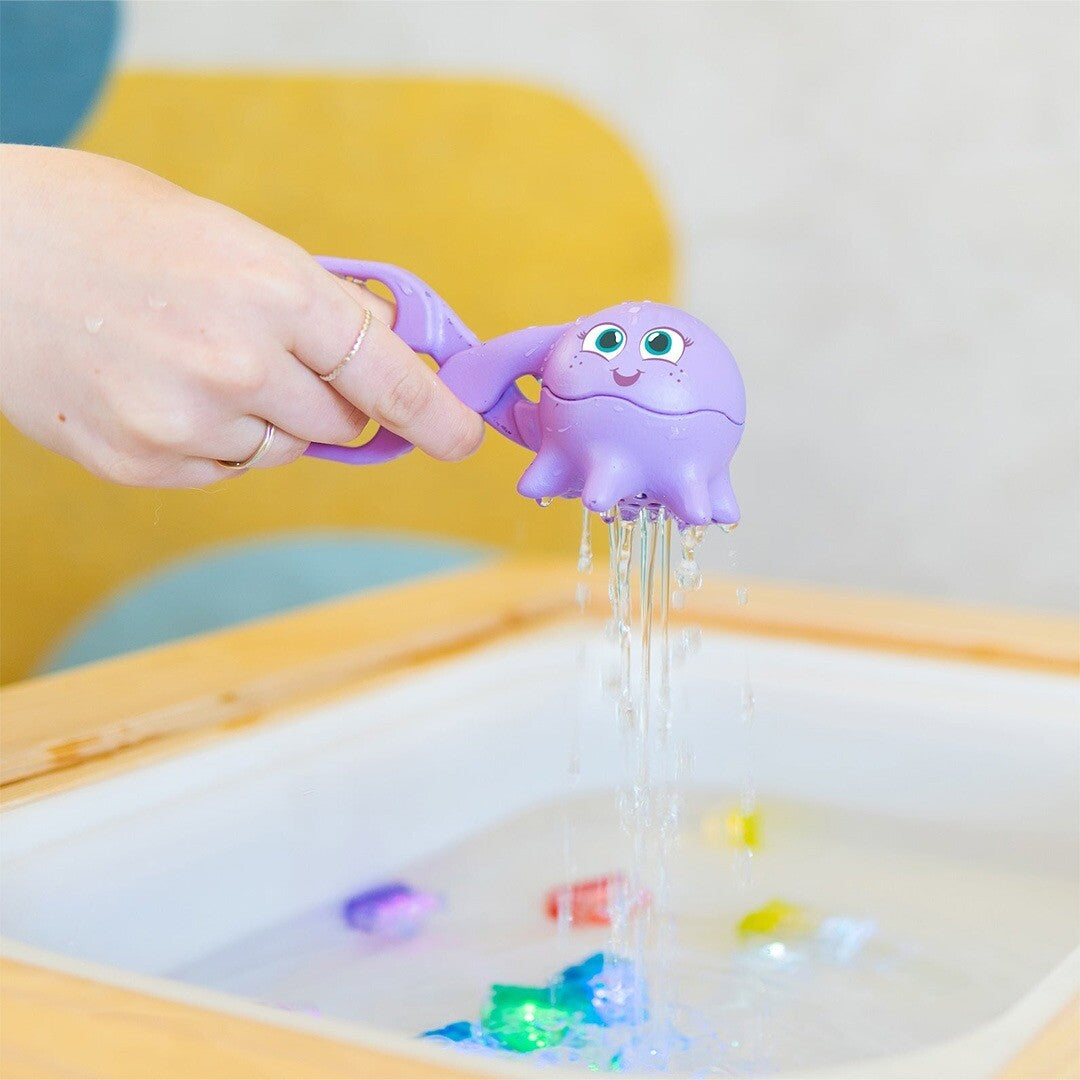 Een hand giet water uit de paarse glo pals octopus scooper in een witte speelbak.