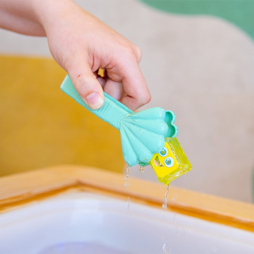 Een hand pakt met de groene glo pals tang een geel lichtgevend blokje uit het water.