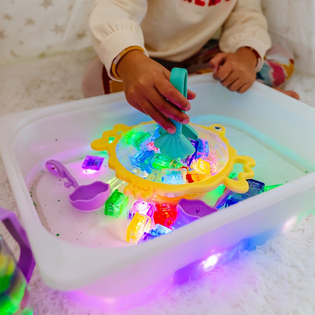 Een kind gebruikt de groene glo pals tang om lichtgevende blokjes uit de gele krab-zeef in een waterbak te pakken.