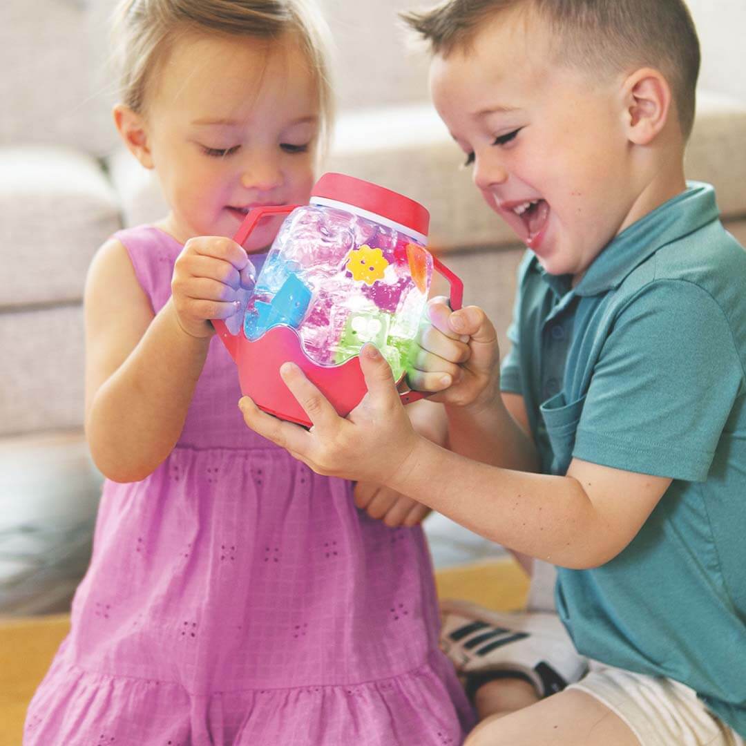 Twee kinderen houden samen een rood gloeiende glo pals sensorische speelbeker met gekleurde vormen vast.