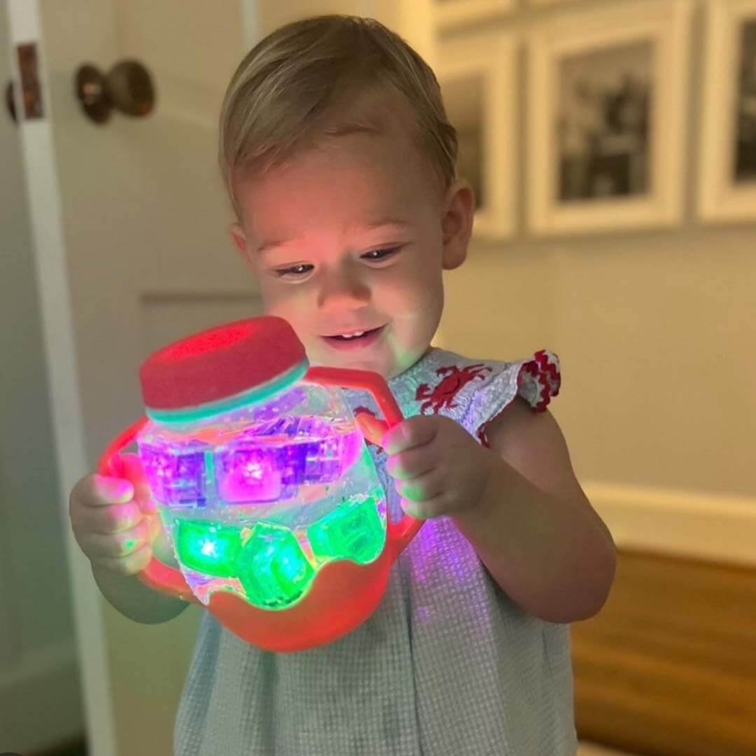 Een peuter houdt een gloeiende rode glo pals sensorische speelbeker vast met veelkleurige lichtjes.