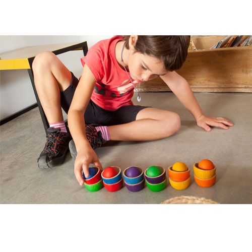 Een kind speelt met Grapat houten sorteer- en stapelspeelgoed van bakjes en ballen in regenboogkleuren.