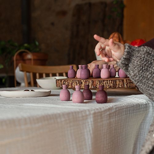 Een kind speelt met grapat houten speelfiguren in roze-paarse tinten op een houten schijf aan tafel.