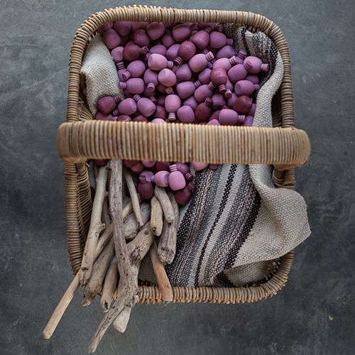 Een rieten mand gevuld met grapat houten speelfiguren in roze-paarse tinten, drijfhout en een gestreepte doek.