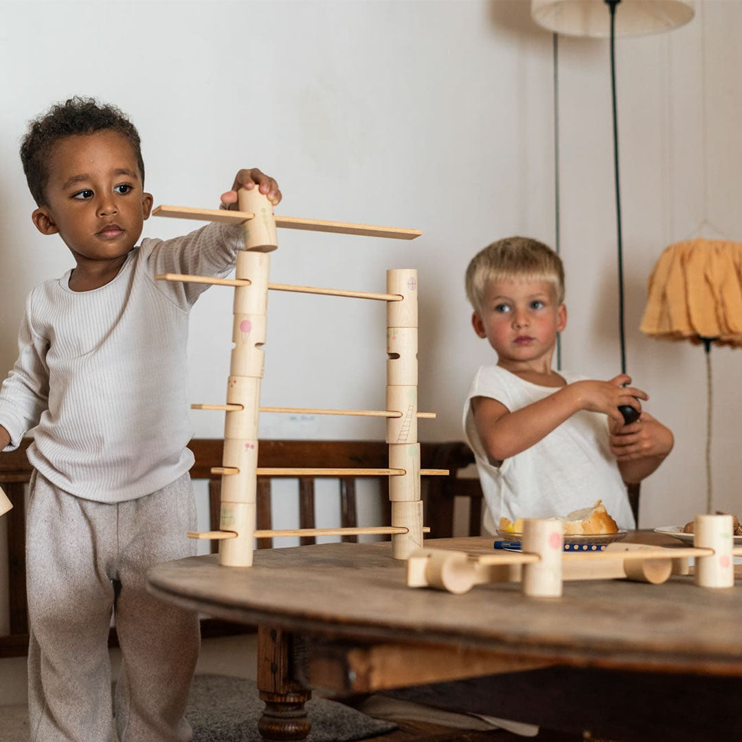 Twee kinderen spelen met de Grapat houten bouwset aan een tafel in een huiselijke omgeving.