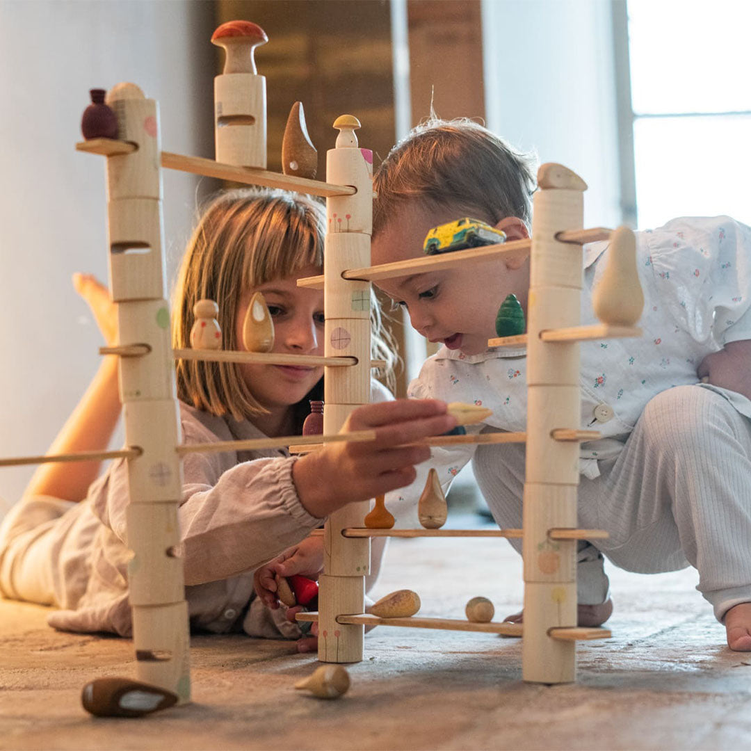 Twee kinderen spelen op de grond met de Grapat houten bouwset en kleine houten figuren.