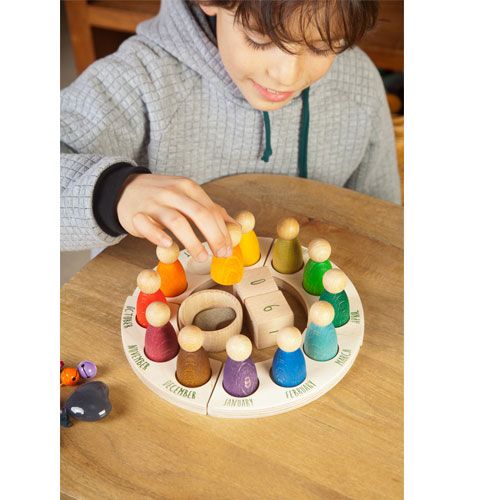 Een kind plaatst een geel houten poppetje in de Grapat houten eeuwige kalender met maanden en andere gekleurde poppetjes.