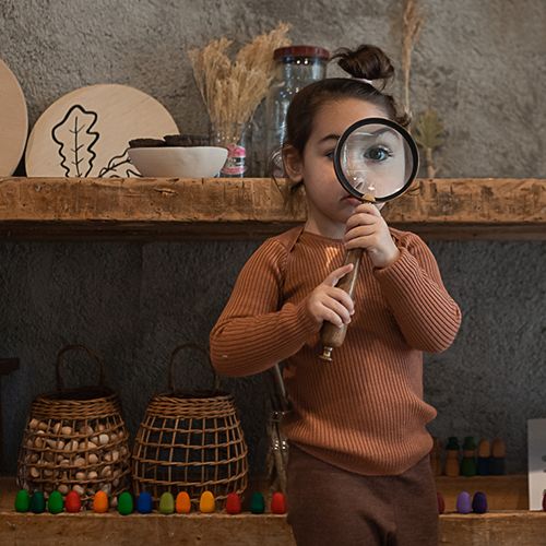 Een kind kijkt door een vergrootglas, met op de achtergrond kleurrijke Grapat houten speelgoed eieren.