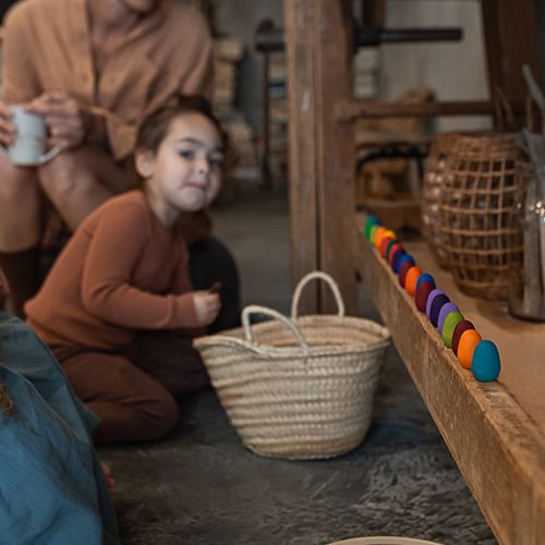 Een kind kijkt naar een rij kleurrijke Grapat houten speelgoed eieren op een houten plank.