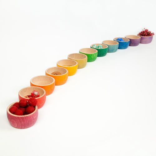 Een rij Grapat houten bakjes in regenboogkleuren, gevuld met kleine speelvoorwerpen.