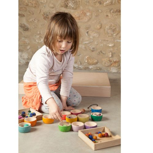 Een kind speelt met Grapat houten bakjes en sorteert kleine voorwerpen.