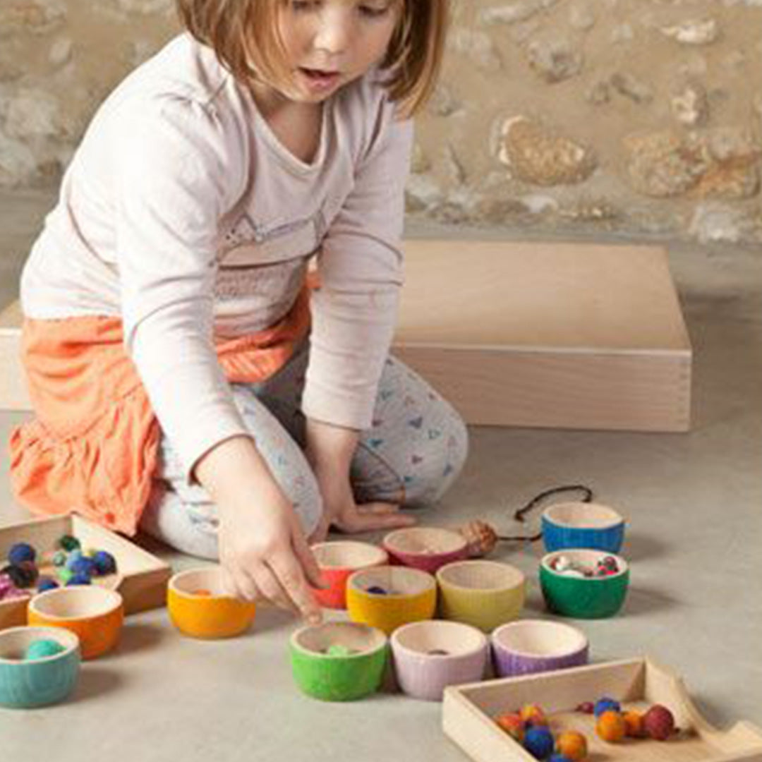 Een kind speelt met de Grapat houten bakjes en sorteert kleine balletjes.