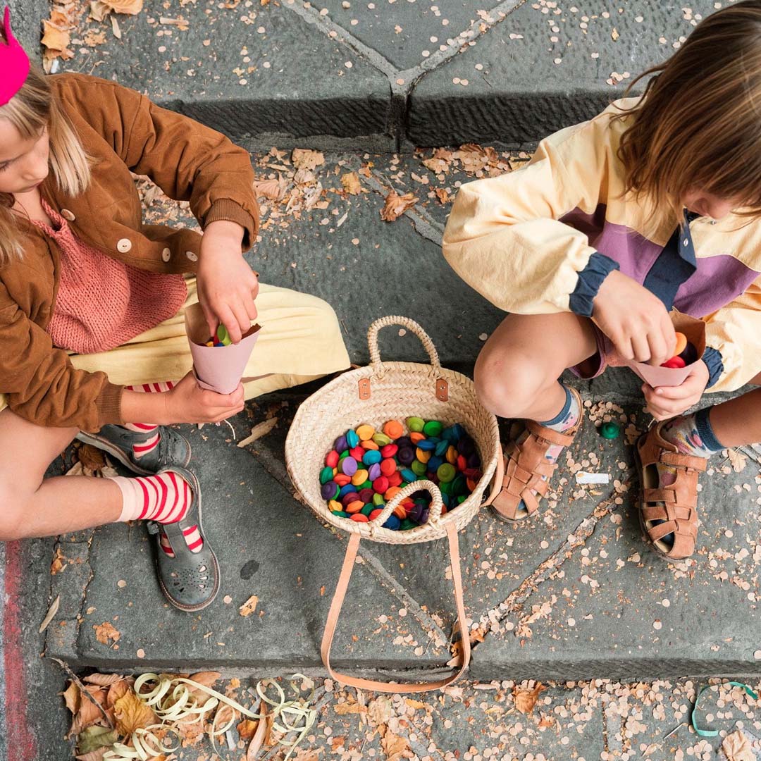 Twee kinderen spelen buiten met de kleurrijke houten bloemen uit een rieten mand.
