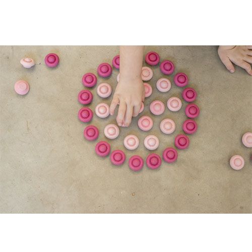 Een kind hand rangschikt Grapat houten speelgoedbloemen in roze tinten tot een cirkel op de grond.