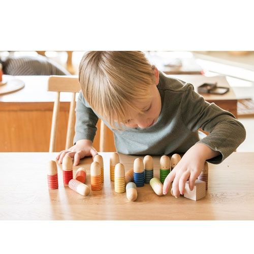 Een jongen speelt met de grapat houten brots poppetjes op een houten tafel.