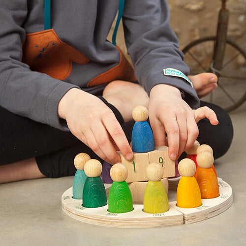 Een kind speelt met de Grapat houten eeuwige kalender en plaatst een blauwe peg doll op de datumblokjes.