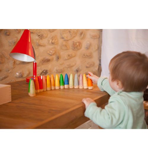 Een baby reikt naar een rij Grapat houten figuren die op een houten tafel staan.