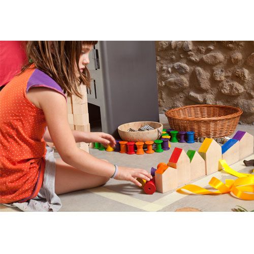 Een kind speelt op de grond met Grapat houten huisjes en een houten treintje.