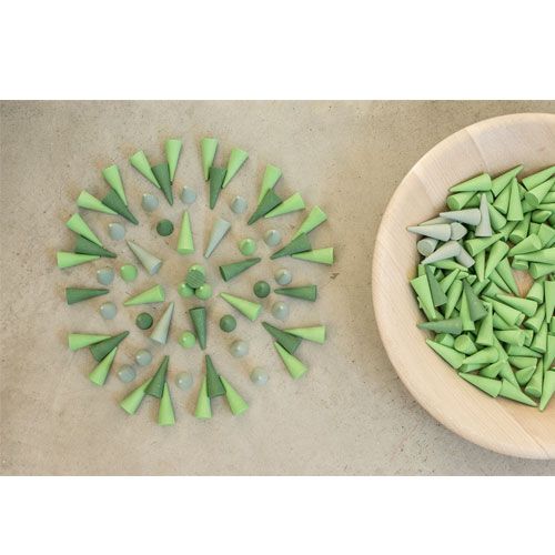 Grapat houten kegels in groene en grijsgroene tinten, deels gerangschikt in een cirkel en deels in een houten kom.