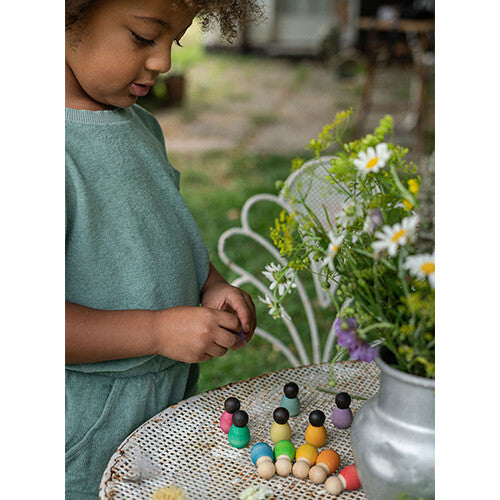 Een kind kijkt naar grapat houten nins® poppetjes baby's die op een witte tuintafel staan.
